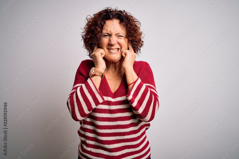 Middle age beautiful curly hair woman wearing casual striped sweater over white background covering ears with fingers with annoyed expression for the noise of loud music. Deaf concept.