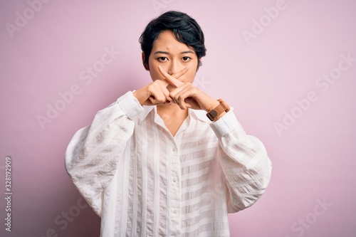 Young beautiful asian girl wearing casual shirt standing over isolated pink background Rejection expression crossing fingers doing negative sign