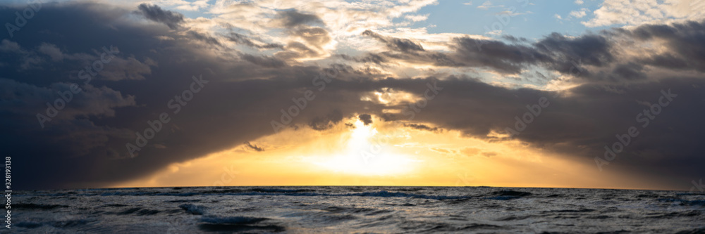beautiful sunset over the sea, panorama view of a dramatic sunset with dark clouds forming a bridge. panorama with rain clouds or storm clouds before the storm, background for websites or banners
