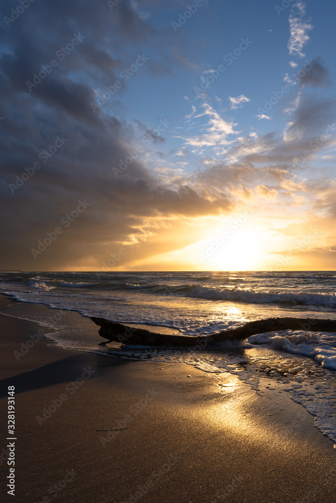 beautiful sunset over the sea, panorama view of a dramatic sunset with dark clouds. rain clouds or storm clouds before the storm, tree trunk lies in the water on the bea