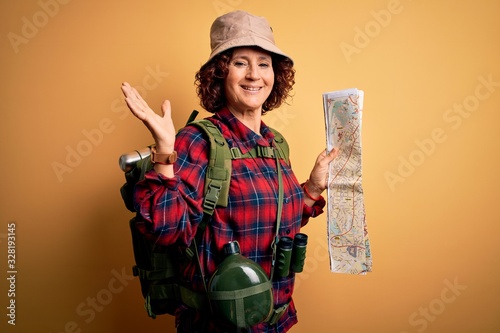Middle age curly hair hiker woman hiking wearing backpack and water canteen holding city map very happy and excited, winner expression celebrating victory screaming with big smile and raised hands photo