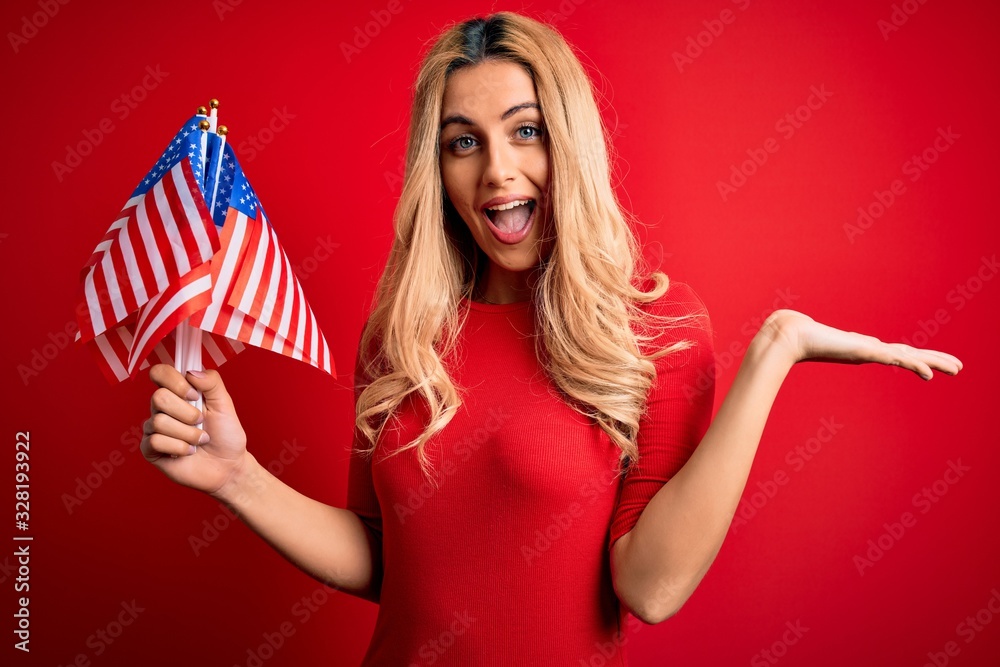 Beautiful blonde patriotic woman holding united states flags celebrating independence day very happy and excited, winner expression celebrating victory screaming with big smile and raised hands Beautiful blonde patriotic woman holding united states flags celebrating independence day very happy and excited, winner expression celebrating victory screaming with big smile and raised hands