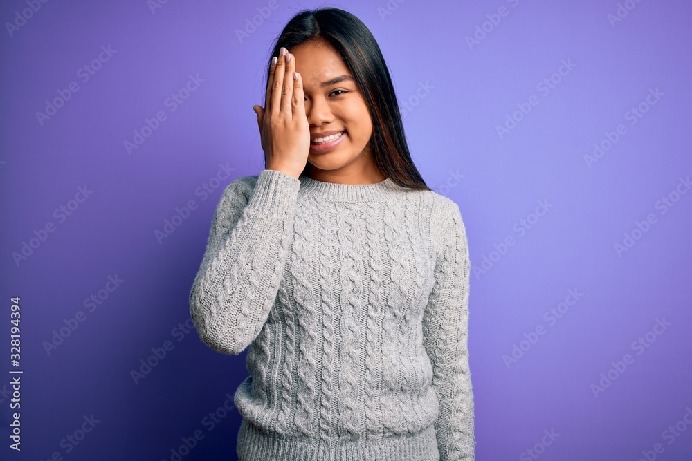 Young beautiful asian girl wearing casual sweater standing over isolated purple background covering one eye with hand, confident smile on face and surprise emotion. Young beautiful asian girl wearing casual sweater standing over isolated purple background covering one eye with hand, confident smile on face and surprise emotion.