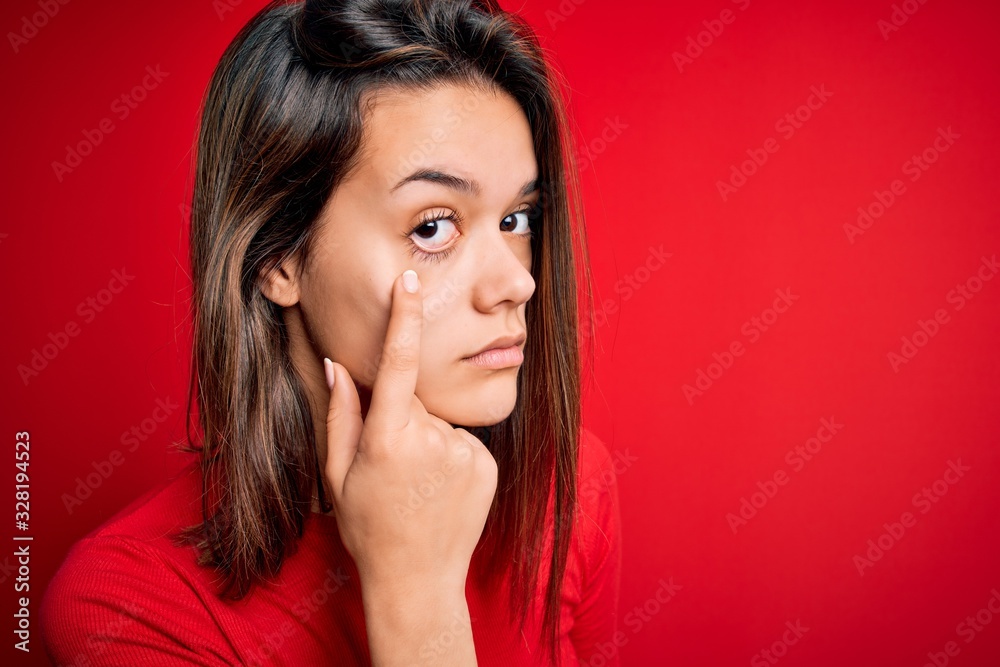 Young beautiful brunette girl wearing casual t-shirt over isolated red background Pointing to the eye watching you gesture, suspicious expression Young beautiful brunette girl wearing casual t-shirt over isolated red background Pointing to the eye watching you gesture, suspicious expression