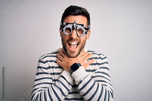Young handsome man with beard wearing optometry glasses over isolated white background shouting and suffocate because painful strangle. Health problem. Asphyxiate and suicide concept.