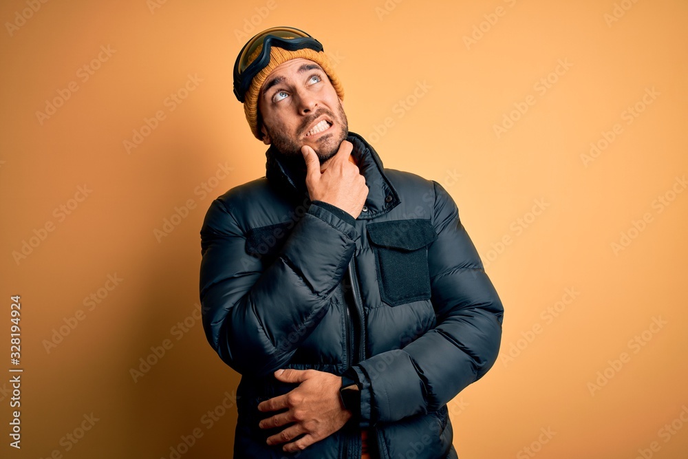 Young handsome skier man with beard wearing snow sportswear and ski goggles Thinking worried about a question, concerned and nervous with hand on chin Young handsome skier man with beard wearing snow sportswear and ski goggles Thinking worried about a question, concerned and nervous with hand on chin