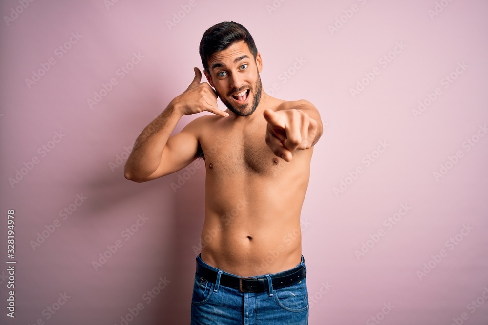 Young handsome strong man with beard shirtless standing over isolated pink background smiling doing talking on the telephone gesture and pointing to you. Call me.