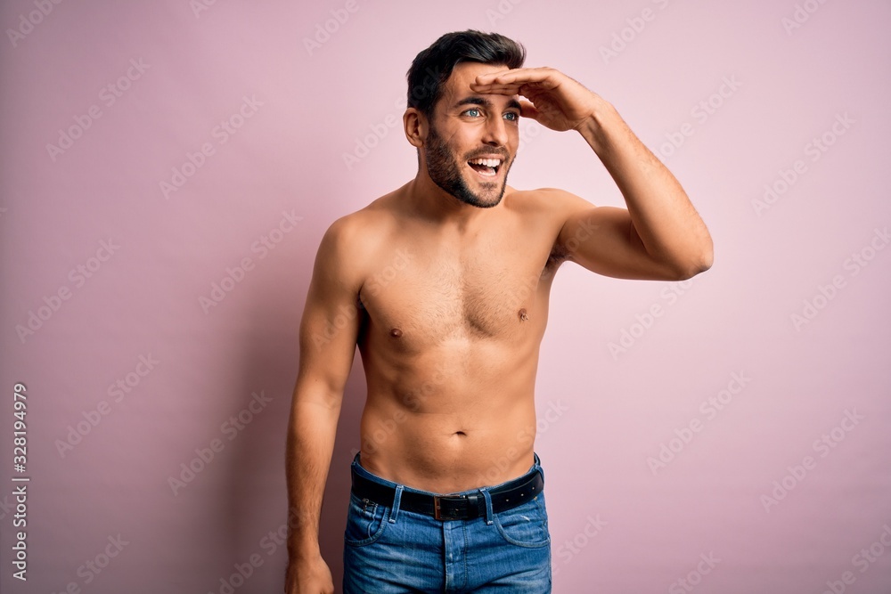 Young handsome strong man with beard shirtless standing over isolated pink background very happy and smiling looking far away with hand over head. Searching concept. Young handsome strong man with beard shirtless standing over isolated pink background very happy and smiling looking far away with hand over head. Searching concept.