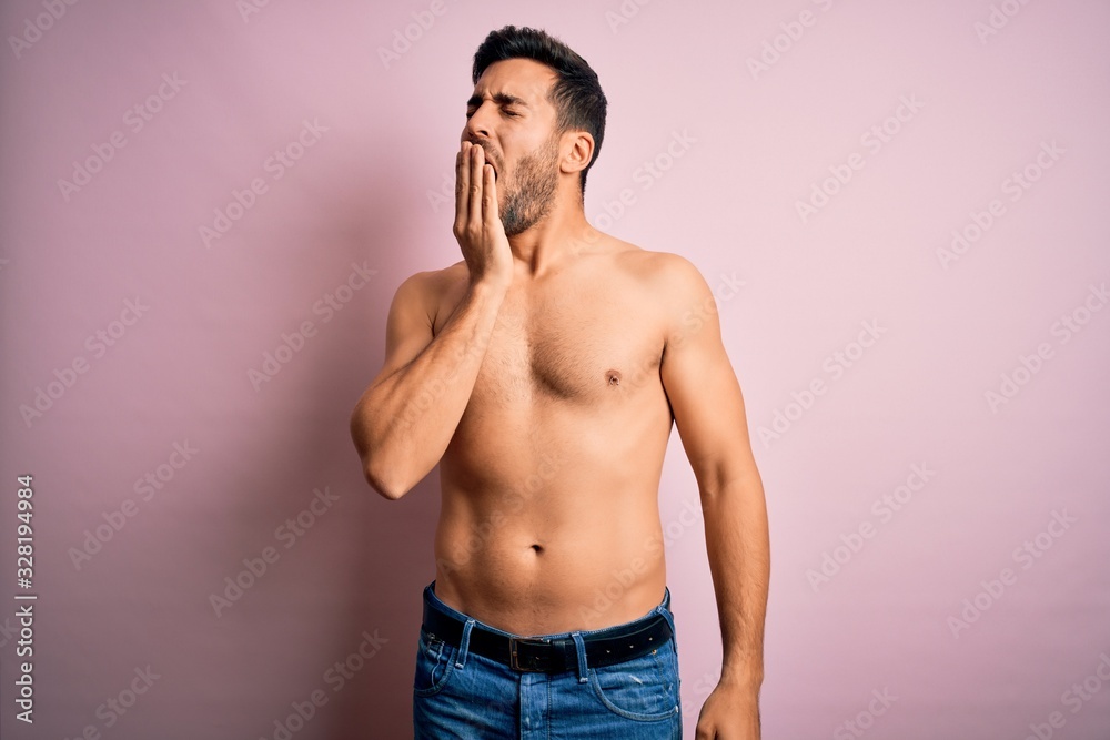 Fototapeta premium Young handsome strong man with beard shirtless standing over isolated pink background bored yawning tired covering mouth with hand. Restless and sleepiness.