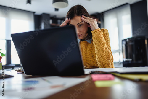 Young worried entrepreneur woman looking at laptop computer at home
