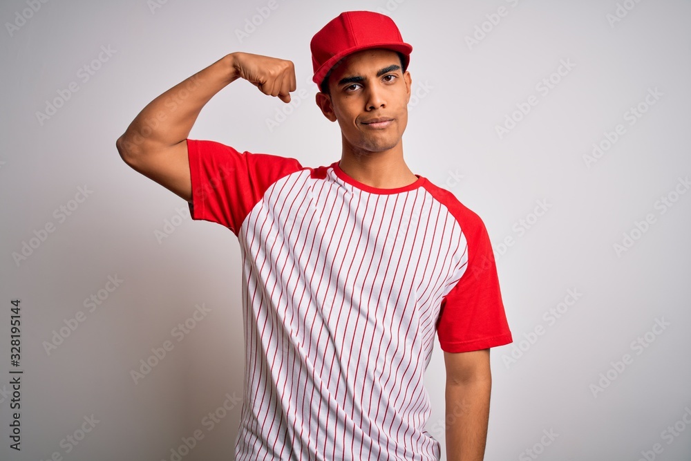 Young handsome african american sportsman wearing striped baseball t-shirt and cap Strong person showing arm muscle, confident and proud of power Young handsome african american sportsman wearing striped baseball t-shirt and cap Strong person showing arm muscle, confident and proud of power