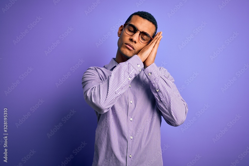 Handsome african american man wearing striped shirt and glasses over purple background sleeping tired dreaming and posing with hands together while smiling with closed eyes. Handsome african american man wearing striped shirt and glasses over purple background sleeping tired dreaming and posing with hands together while smiling with closed eyes.