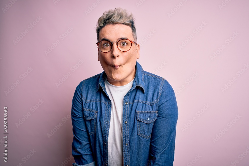 Young handsome modern man wearing glasses and denim jacket over pink isolated background making fish face with lips, crazy and comical gesture. Funny expression. Young handsome modern man wearing glasses and denim jacket over pink isolated background making fish face with lips, crazy and comical gesture. Funny expression.