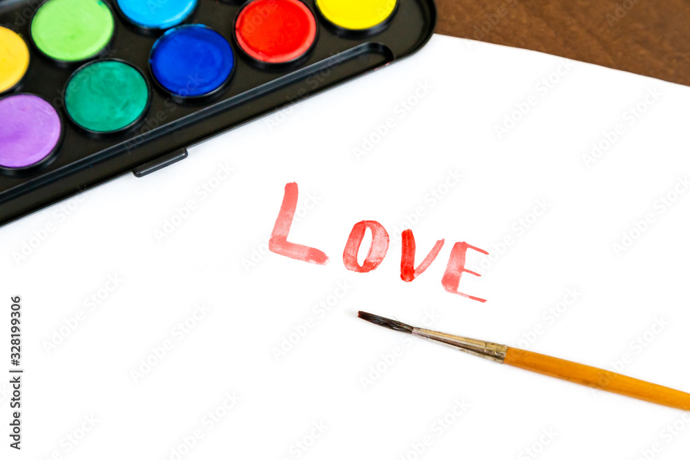 Handwritten LOVE text with brush and watercolor paints on white background. Box of watercolor paints with a brush for drawing. Love concept Handwritten LOVE text with brush and watercolor paints on white background. Box of watercolor paints with a brush for drawing. Love concept