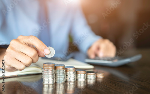 Businessman writing notes in documents with car model on stack of coins, in business concept