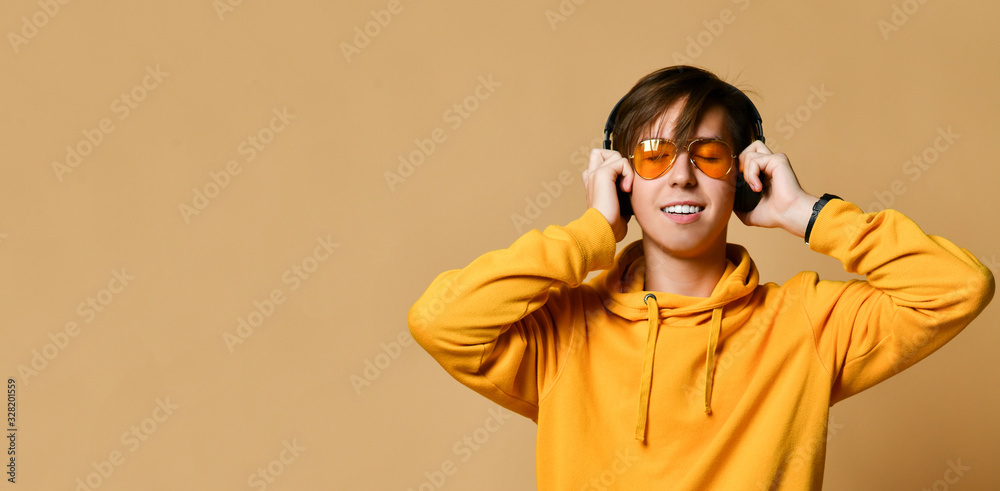 Young positive teen boy in yellow hoodie, sunglasses and headphones standing and smiling Young positive teen boy in yellow hoodie, sunglasses and headphones standing and smiling