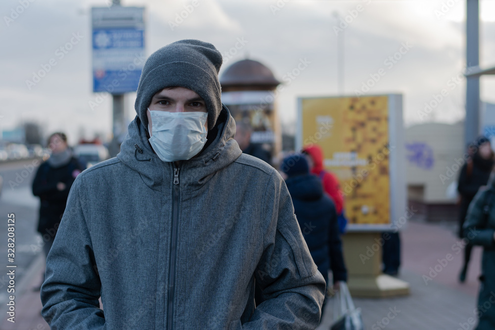 Man in the city. on the face a protective rag mask. remedy against viruses and diseases. protection against coronovirus. There are many passers-by on the street. Bus stop Man in the city. on the face a protective rag mask. remedy against viruses and diseases. protection against coronovirus. There are many passers-by on the street. Bus stop