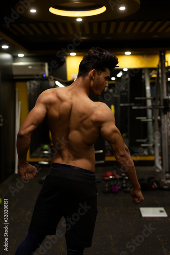 An young and handsome Indian Bengali brunette man with muscular body showing his muscular backside while exercising in a multi gym. Fitness and Indian lifestyle.