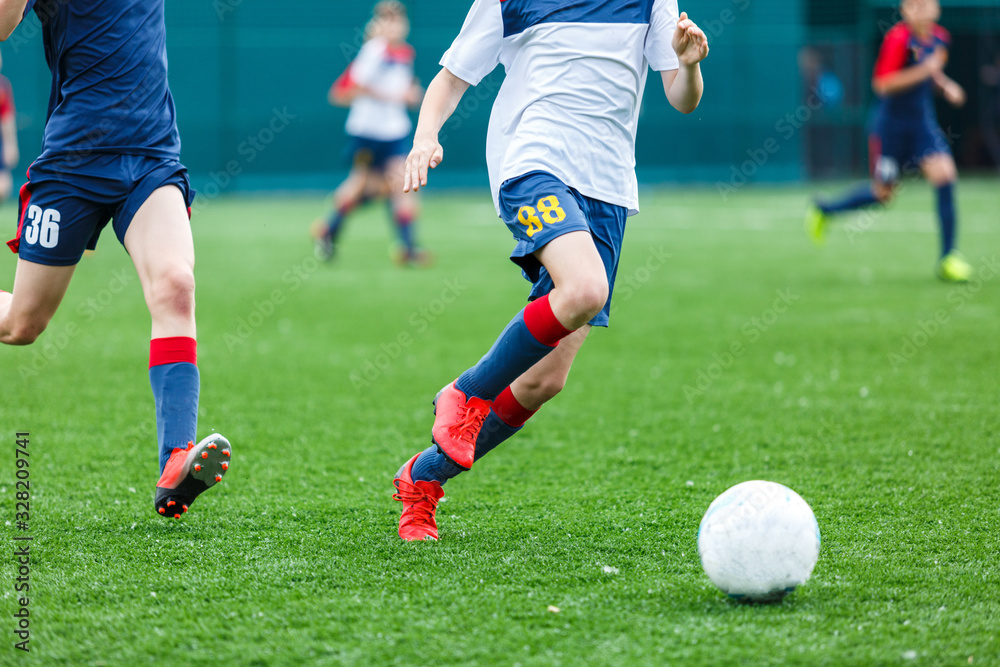 Boys in white and blue sportswear plays  football on field, dribbles ball. Young soccer players with ball on green grass. Training, football, active lifestyle for kids concept 