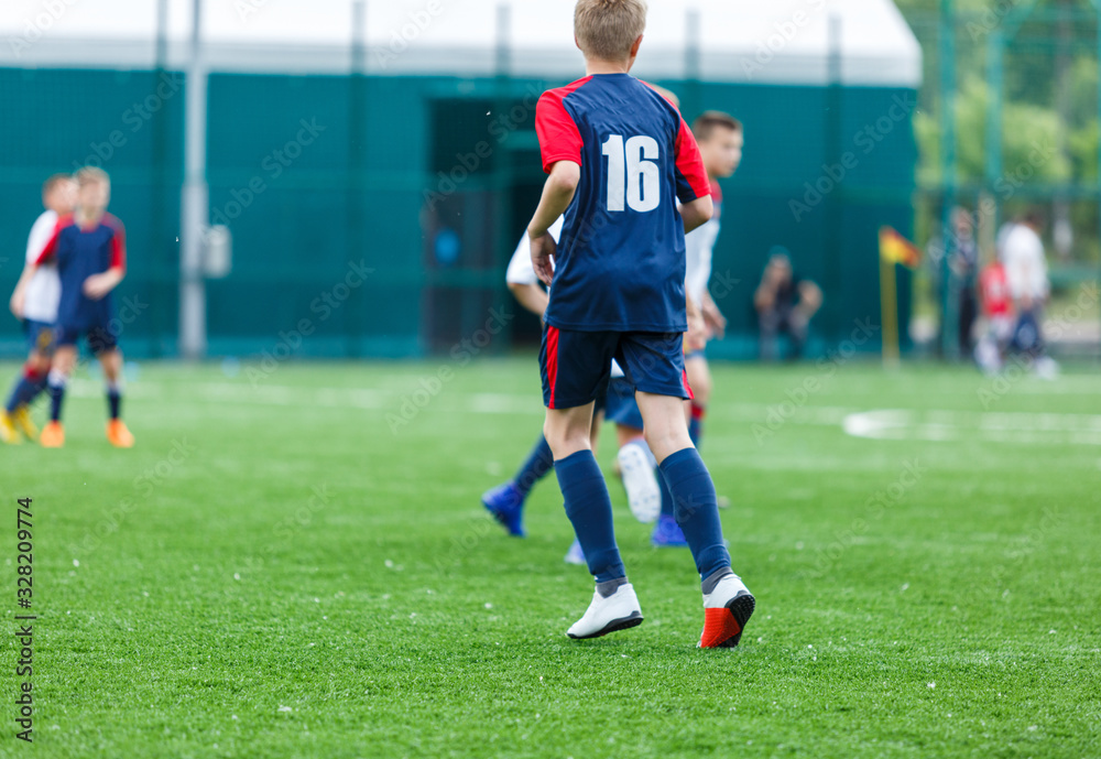 Boys in white and blue sportswear plays  football on field, dribbles ball. Young soccer players with ball on green grass. Training, football, active lifestyle for kids concept 