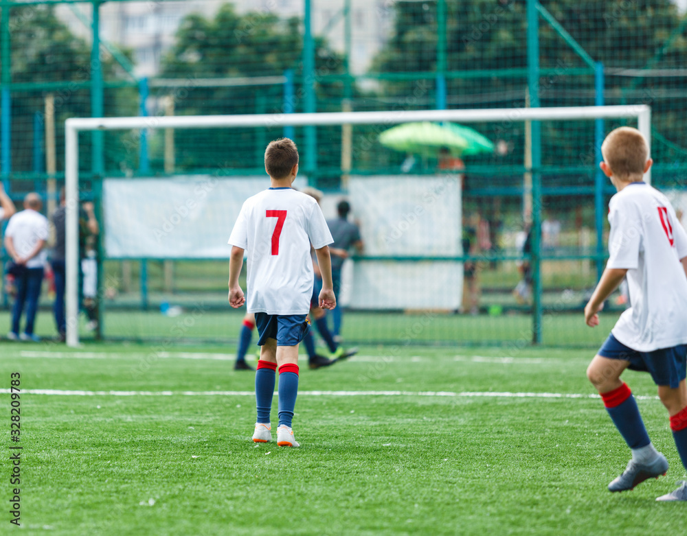 Boys in white and blue sportswear plays  football on field, dribbles ball. Young soccer players with ball on green grass. Training, football, active lifestyle for kids concept 