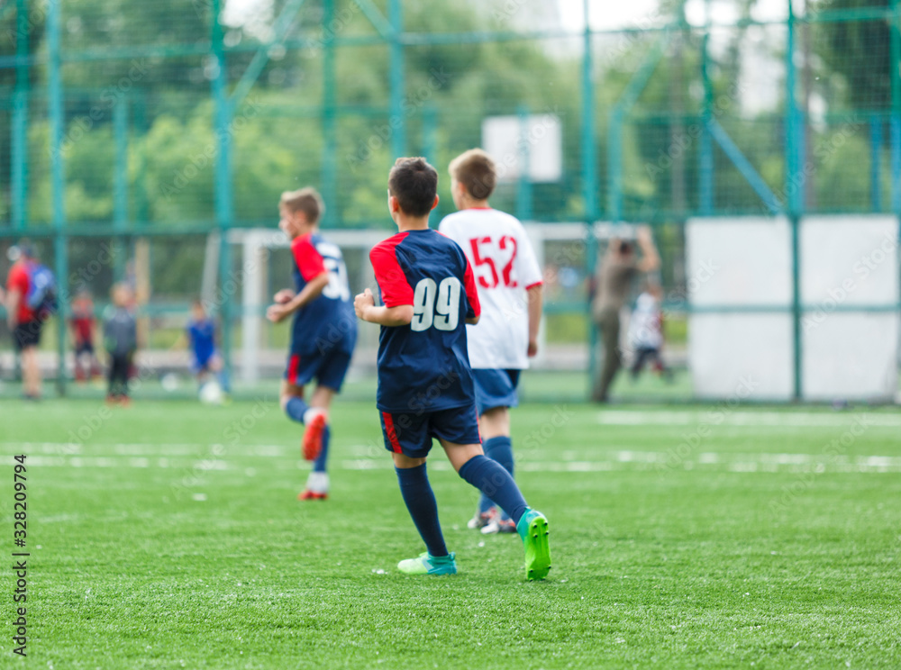 Obraz premium Boys in white and blue sportswear plays football on field, dribbles ball. Young soccer players with ball on green grass. Training, football, active lifestyle for kids concept 
