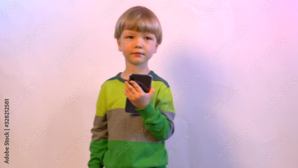 Cute blond boy in green sweater at home. a teenager took smartphone and sings Cute blond boy in green sweater at home. a teenager took smartphone and sings