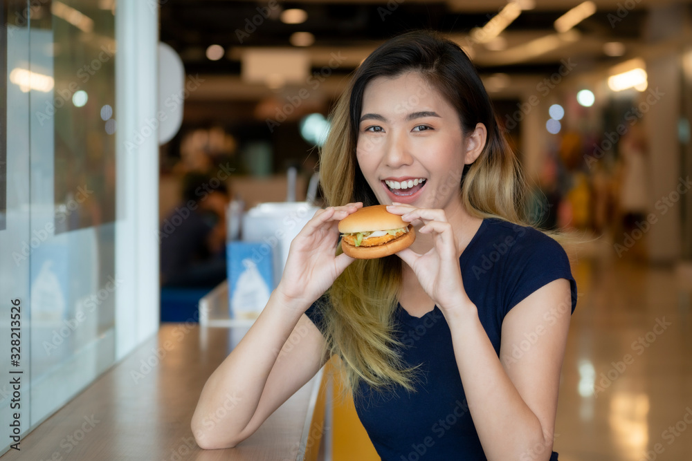An Asian woman wearing a blue shirt is about to eat a hamburger. An Asian woman wearing a blue shirt is about to eat a hamburger.