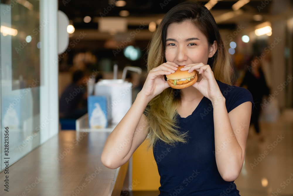 An Asian woman wearing a blue shirt is about to eat a hamburger. An Asian woman wearing a blue shirt is about to eat a hamburger.