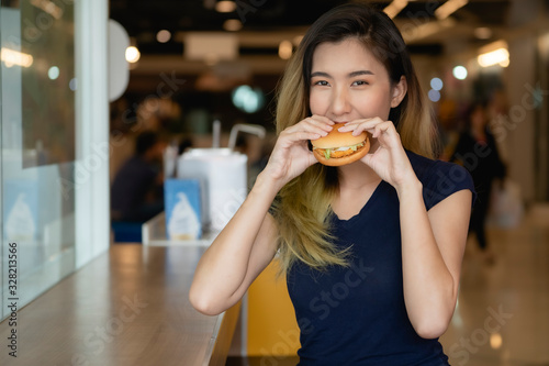 An Asian woman wearing a blue shirt is about to eat a hamburger.