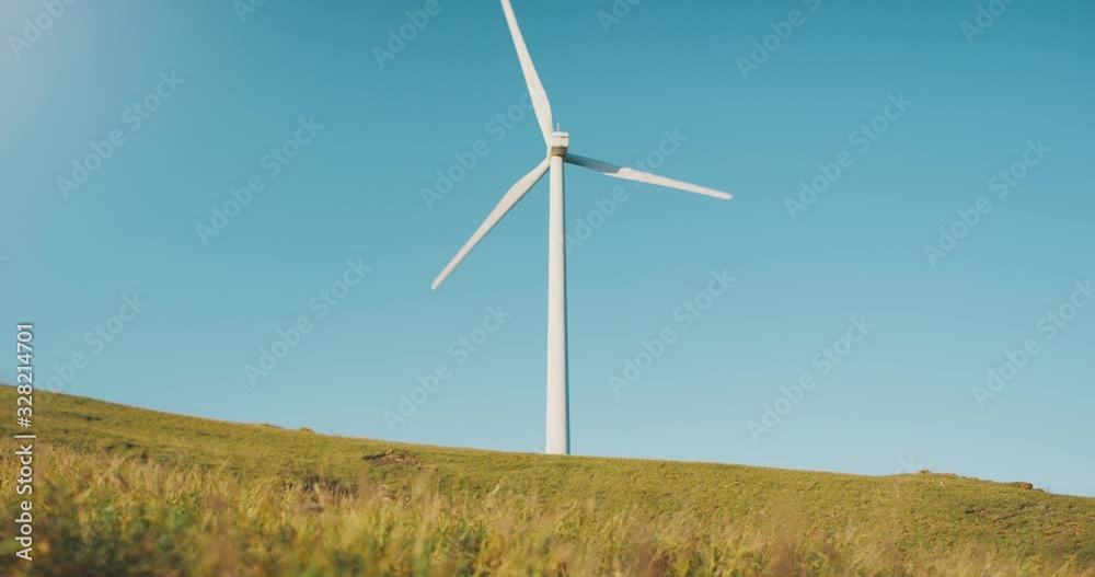 Wind turbine spinning in the late afternoon surrounded by golden yellow fields with a clear blue sky in the background Wind turbine spinning in the late afternoon surrounded by golden yellow fields with a clear blue sky in the background