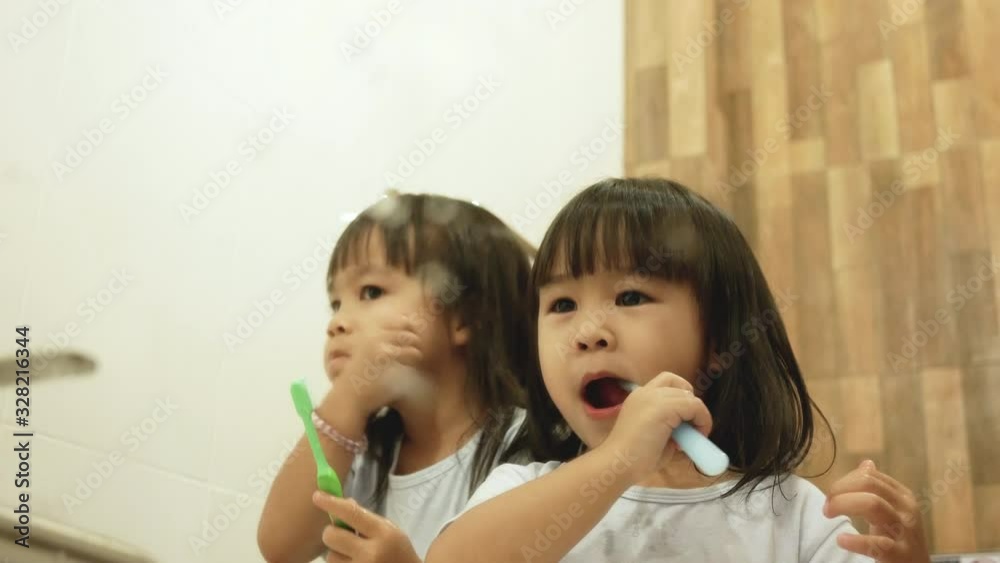 Happy sibling little child girls brushing teeth together in the bathroom. Oral hygiene concept.
