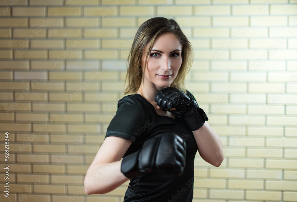 Girl and Boxing. Portrait of a girl in sportswear in Boxing gloves , mix mma open fingers gloves  against a light brown brick wall. The girl looks at the camera