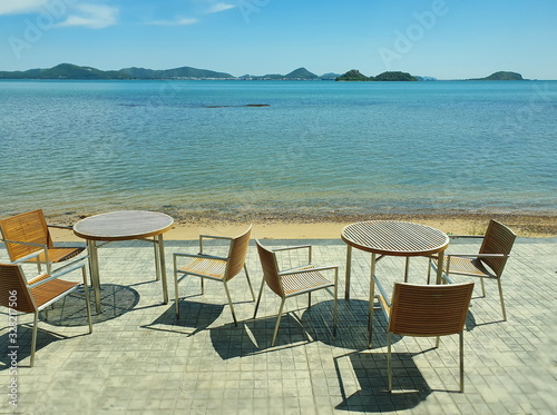Outdoor chairs and tables for dining or coffee in front of the blue sea, blue sky and green mountains. During the sunny day