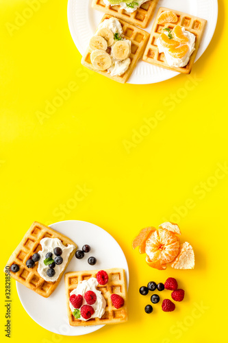 Beautiful yummy snacks. Waffles with cream and friuits on yellow background top-down frame copy space