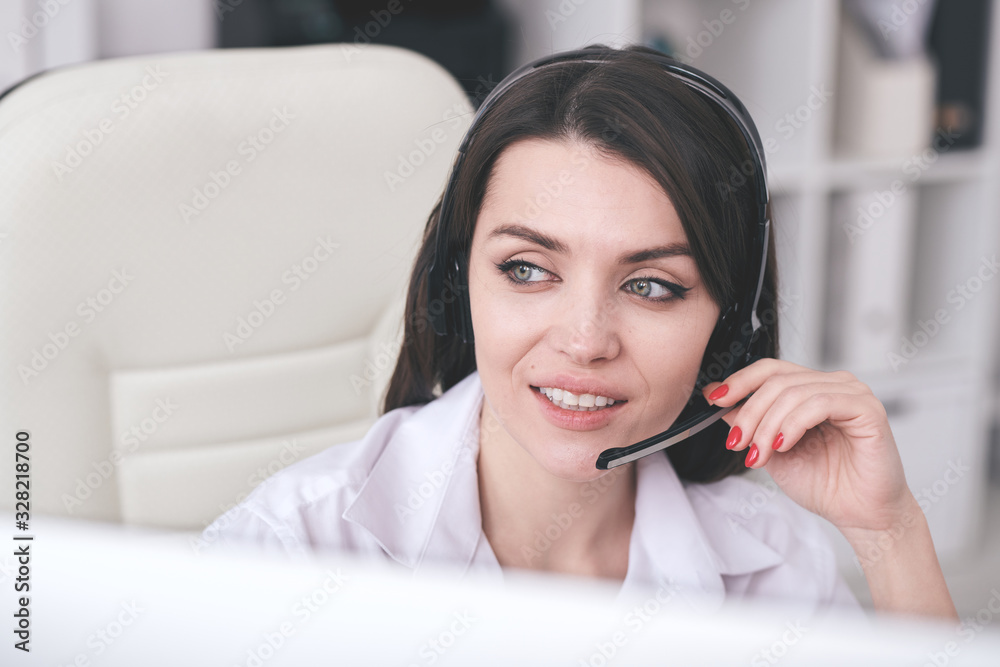 Positive attractive young female call center operator in hands-free microphone answering questions of people Positive attractive young female call center operator in hands-free microphone answering questions of people
