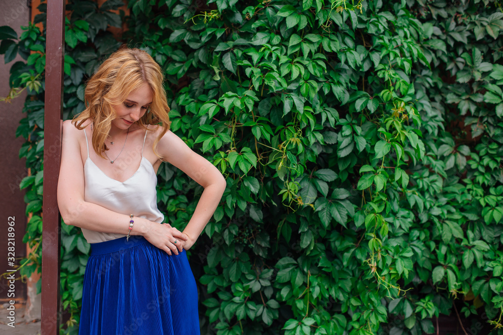 Portrait of a young beautiful woman, standing next to the wall of wild grape leaves.