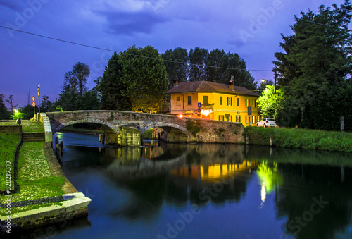 medieval stone bridge with two arches in a countryside location on the outskirts of Milan. night view of the river.