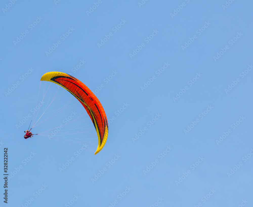 Orange and yellow paraglider on clear blue sky Orange and yellow paraglider on clear blue sky