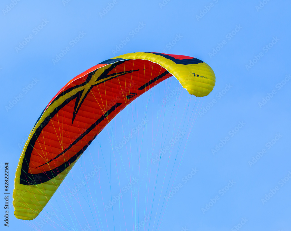 Orange and yellow paraglider on clear blue sky Orange and yellow paraglider on clear blue sky