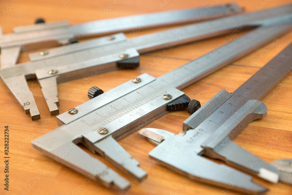 Calipers are on a wooden surface close-up; some objects are out of focus. Shallow depth of field. Measuring tool Calipers are on a wooden surface close-up; some objects are out of focus. Shallow depth of field. Measuring tool