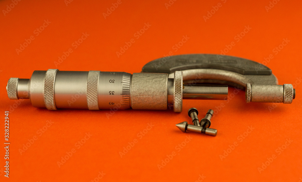 close-up on a bright orange background measuring instrument micrometer with additional inserts. Macro shot, some details out of focus. Precision measuring tool for metalworking close-up on a bright orange background measuring instrument micrometer with additional inserts. Macro shot, some details out of focus. Precision measuring tool for metalworking