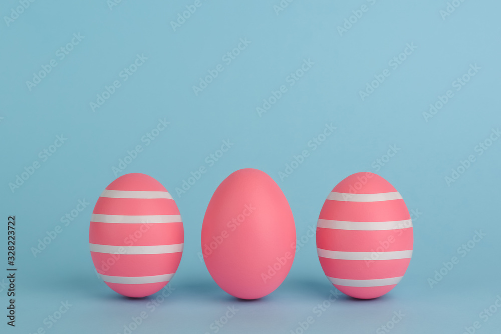 Three Easter decorated pink eggs. Striped pink eggs in a row on a blue background. White strips. Copy space. Pink monochrome Easter concept. Three Easter decorated pink eggs. Striped pink eggs in a row on a blue background. White strips. Copy space. Pink monochrome Easter concept.