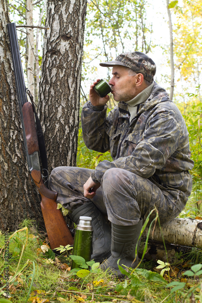 hunter drinks tea from a thermos sitting on a fallen tree