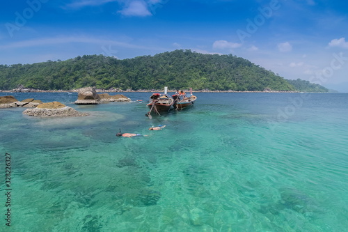 view of tourists snorkeling in blue-green sea and a long-tail boat floating with blue sky background, Ko Jabang, long-tail boat trip from Lipe island, Satun, southern Thailand.