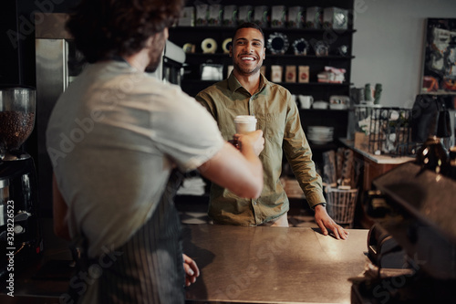 Cheerful customer buying takeaway coffee from modern cafe house standing across counter photo
