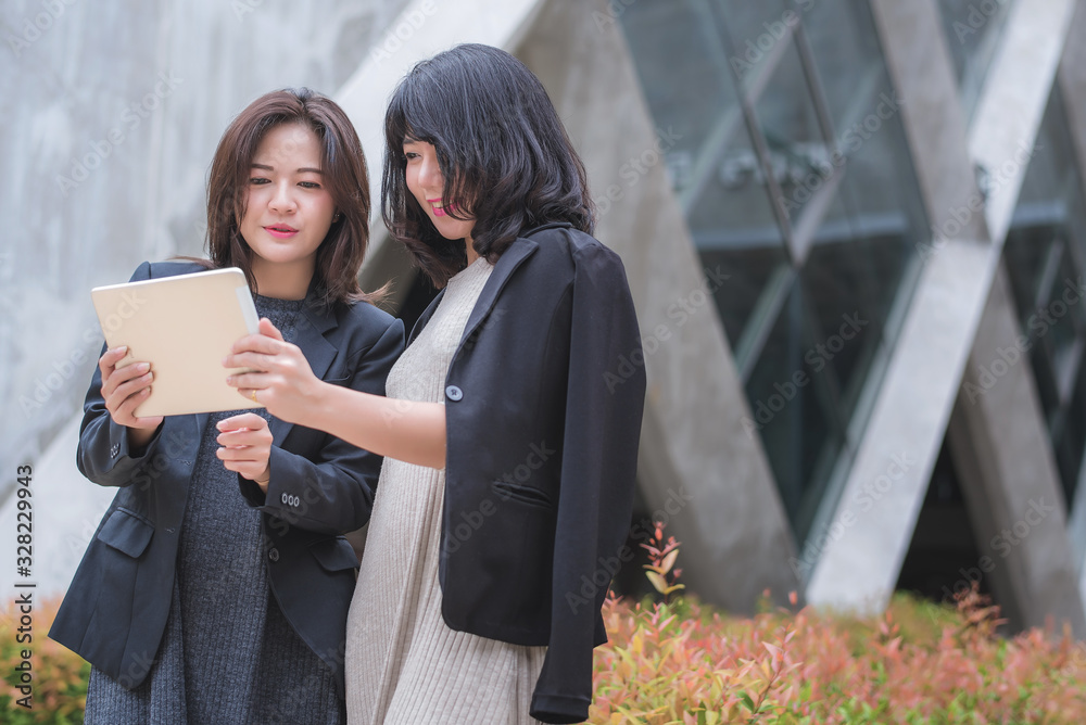 Two businesswoman working together with tablet in front of their office building.