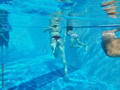 Bodies of mother and small daughter swimming in a pool under water. Woman and girl. Blue color