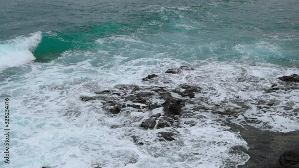 Waves crashing into a rocky formation near the shoreline of a large wave breaking over stones on the sides in slow motion capture at 120fps. Waves crashing into a rocky formation near the shoreline of a large wave breaking over stones on the sides in slow motion capture at 120fps.