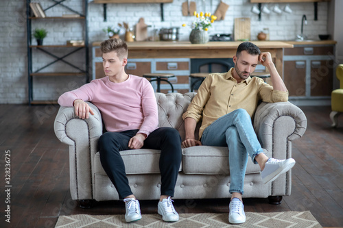 Two men sitting on the sofa not loooking at each other looking upset photo